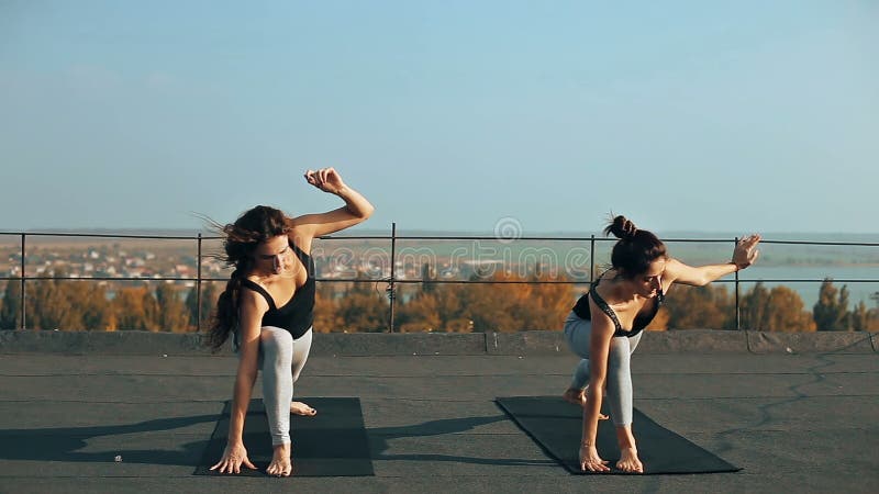 实践瑜伽的两名美丽的妇女在屋顶摆在，户外在早晨