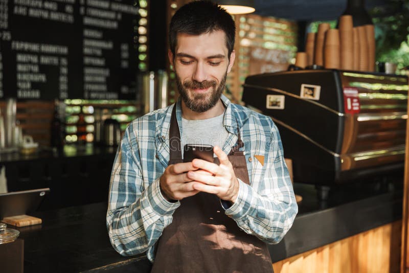 室外白种人barista人键入在街道咖啡馆的手机的或的咖啡馆画象 免版税库存图片