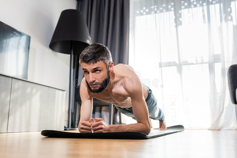 Surface level of shirtless man doing plank on fitness mat at home. Surface level of shirtless man doing plank on fitness mat at home