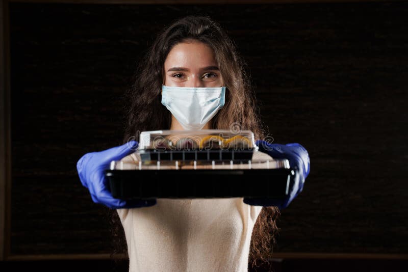 Girl with sushi. Food courier in medical mask. Delivery at quarantine coronavirus covid-19. Young woman holding 2 sushi boxes in hands using gloves. Girl with sushi. Food courier in medical mask. Delivery at quarantine coronavirus covid-19. Young woman holding 2 sushi boxes in hands using gloves