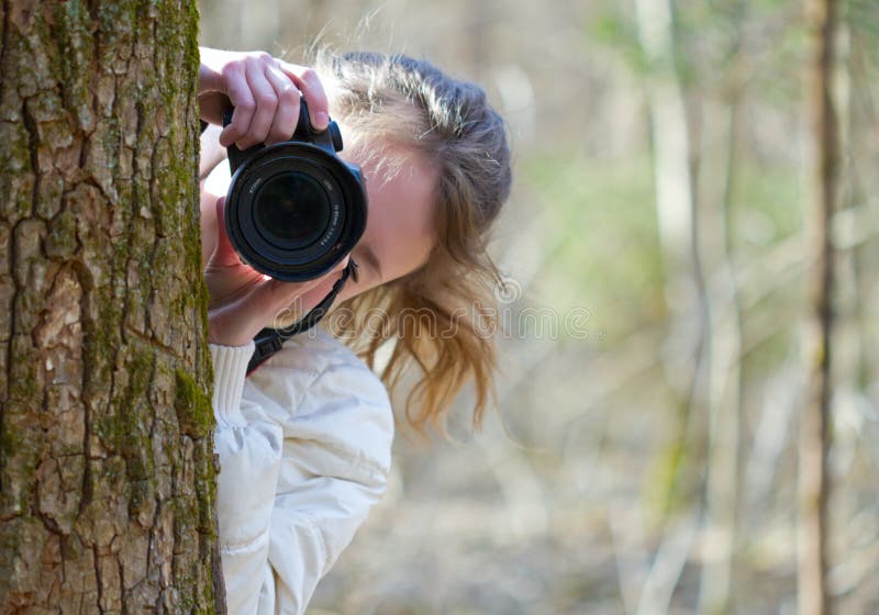 Portrait of nature photographer young woman. The girl is shooting you (camera towarded to you) in a spring day sunny forest. Portrait of nature photographer young woman. The girl is shooting you (camera towarded to you) in a spring day sunny forest.