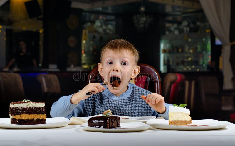 Little boy cannot believe his luck sits dining table holding fork gawping at an array different cakes spread out front of him wonderment. Little boy cannot believe his luck sits dining table holding fork gawping at an array different cakes spread out front of him wonderment