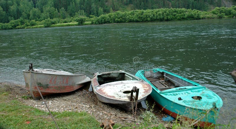 Old fishing boats on the Siberian mountain river Mana against a mountain taiga and rocks. Old fishing boats on the Siberian mountain river Mana against a mountain taiga and rocks.