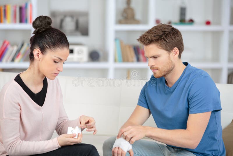 年轻女子用急救包为男友包扎伤口 库存图片