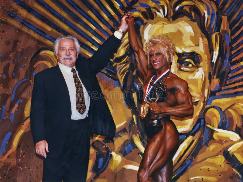 Under the watchful eye of Joe Weider &#x28;in mural&#x29; and the real IFBB head, Kim Chizevsky raises her arm and poses with her first place medal won in the pro women&#x27;s bodybuilding contest at the IFBB Ms Olympia in New York City on November 22, 1997. Kim amazing physique displays superb symmetry, size, and ripped definition. Under the watchful eye of Joe Weider &#x28;in mural&#x29; and the real IFBB head, Kim Chizevsky raises her arm and poses with her first place medal won in the pro women&#x27;s bodybuilding contest at the IFBB Ms Olympia in New York City on November 22, 1997. Kim amazing physique displays superb symmetry, size, and ripped definition.