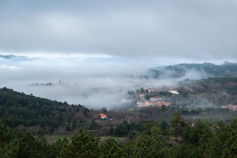 Village surrounded by mountains and forest with low fog covering part of the forest and the village on a cold winter day. Village surrounded by mountains and forest with low fog covering part of the forest and the village on a cold winter day