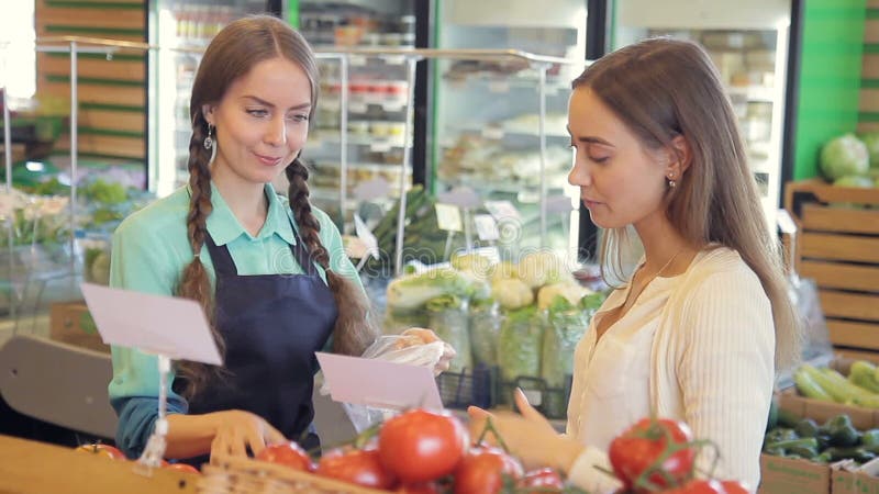 市场雇员帮助包装妇女顾客的蕃茄 在食物部门