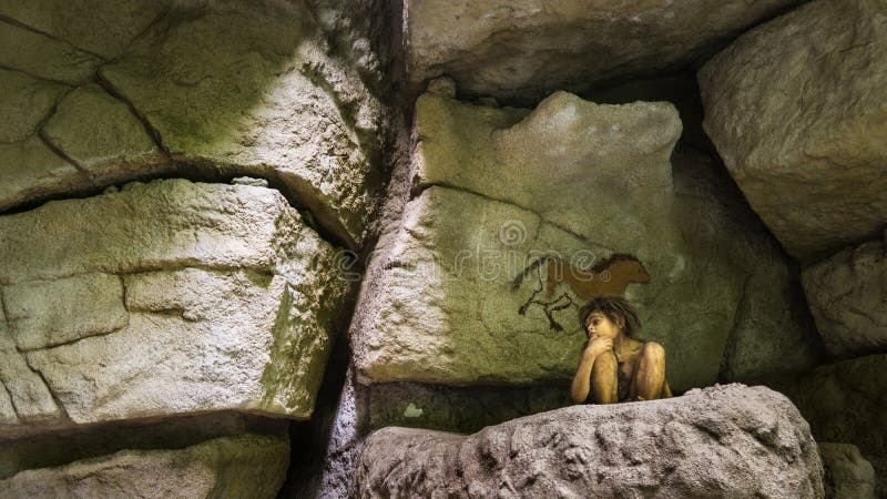 BUDAPEST, HUNGARY - JUN 01, 2018: Museum Exposition - A model of a young caveman boy sitting between the cave art painted rocks. BUDAPEST, HUNGARY - JUN 01, 2018: Museum Exposition - A model of a young caveman boy sitting between the cave art painted rocks.