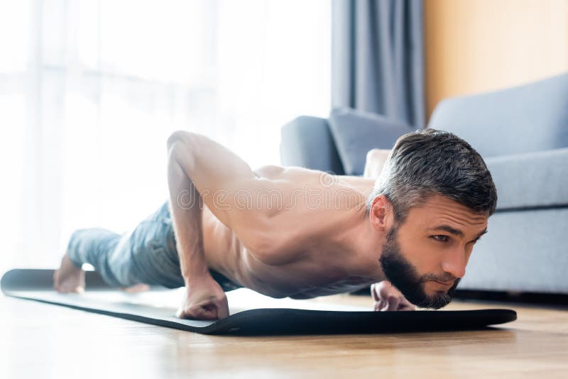 Surface level of handsome shirtless man doing press ups while exercising on fitness mat at home. Surface level of handsome shirtless man doing press ups while exercising on fitness mat at home