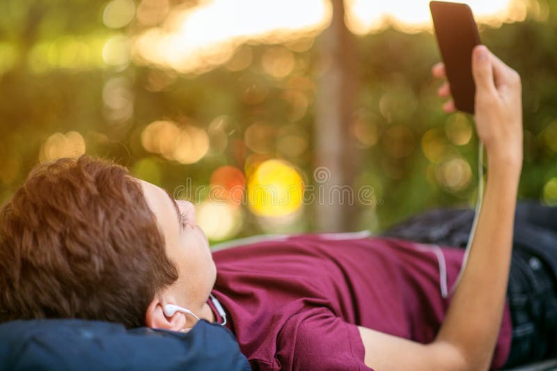 带智能手机的少年躺在公园的长凳上 青少年在户外用手机 白种青少年 库存图片 带智能手机的少年躺在公园的长凳上 青少年在户外用手机 白种青少年 库存图片