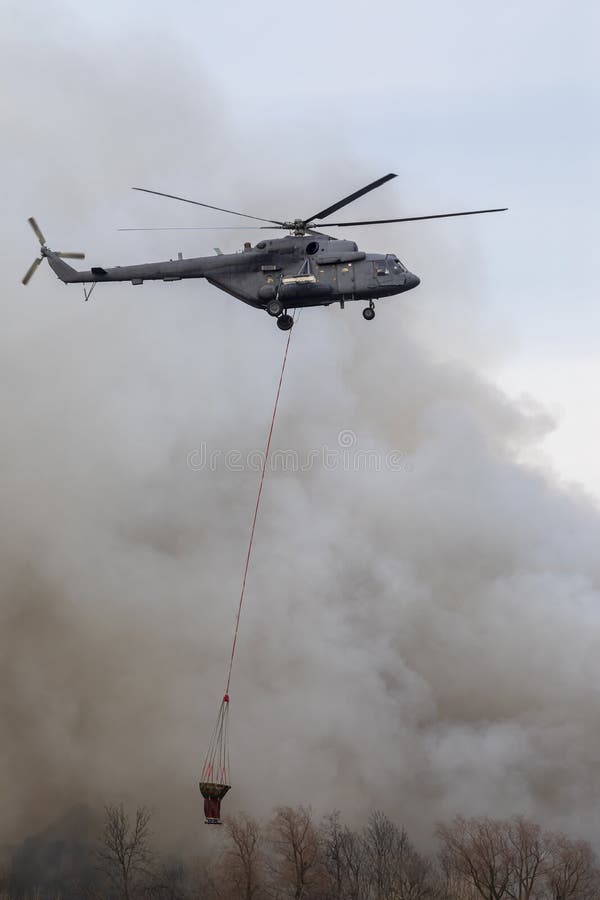 Firefighter helicopter with a water tank in smoke from a fire. Trees in the smoke of a fire. Firefighter helicopter with a water tank in smoke from a fire. Trees in the smoke of a fire