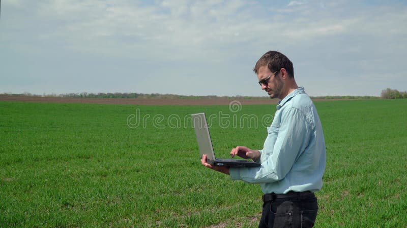 带笔记本电脑的农民检查小麦生长 鲜绿麦田