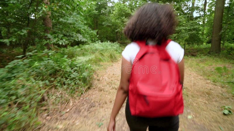 带红色背包、在森林林地里拿着手机的非洲裔女孩远足