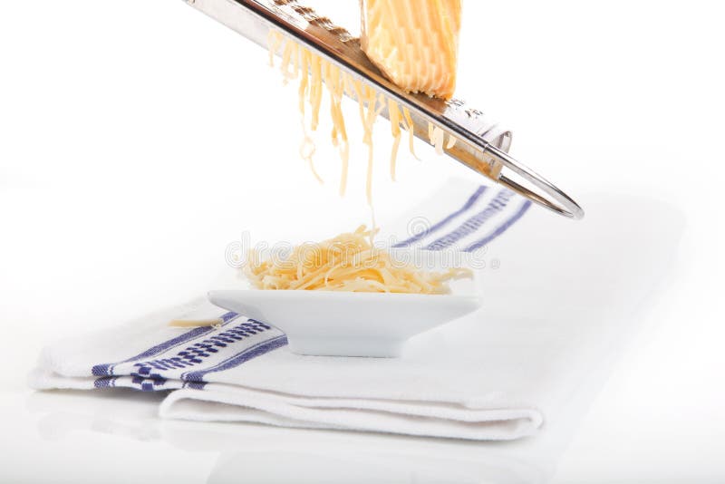 Grated cheese falling into white bowl on kitchen towel isolated on white background. Grated cheese falling into white bowl on kitchen towel isolated on white background.