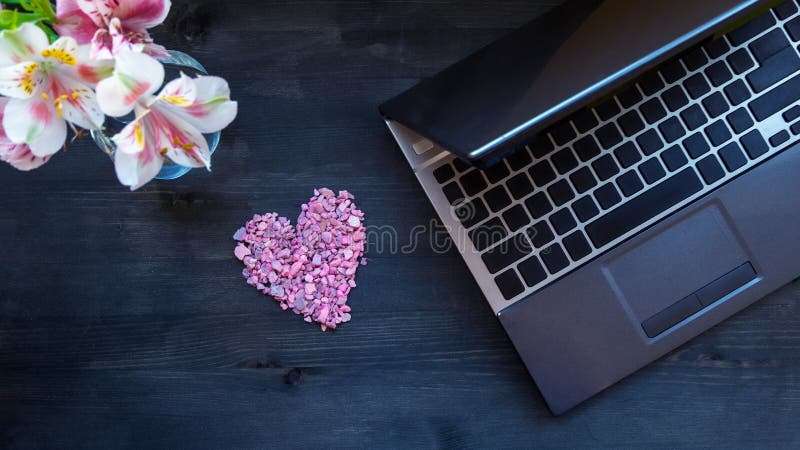 Banner flat lay home office desk. Working at home women workspace with laptop, flowers bouquet and a heart on a dark brown wooden background. Top view feminine background. Banner flat lay home office desk. Working at home women workspace with laptop, flowers bouquet and a heart on a dark brown wooden background. Top view feminine background