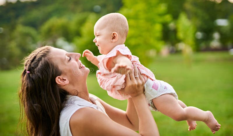 年轻的母亲将她快乐的小女儿举过头顶 免版税库存图片