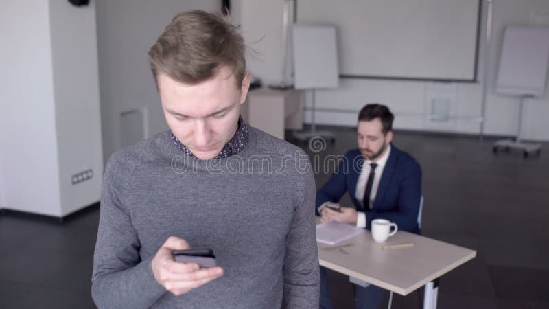 年轻人在现代办公室使用智能手机，站立户内