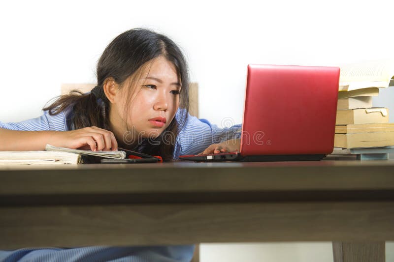 年轻人注重了并且挫败了亚裔韩国学生女孩努力与在被淹没的书桌上的手提电脑和书堆一起使用和 免版税库存图片 年轻人注重了并且挫败了亚裔韩国学生女孩努力与在被淹没的书桌上的手提电脑和书堆一起使用和 免版税库存图片