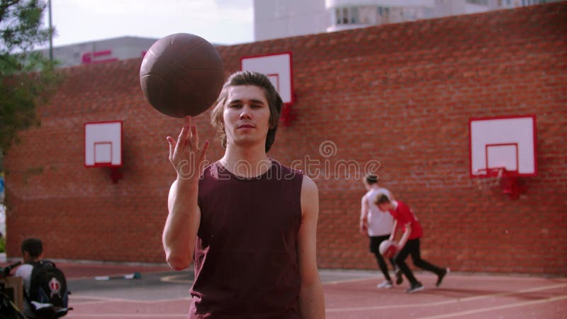 年轻人站在篮球运动场上，把球旋在手指上，然后扔下去