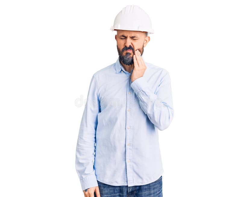 年轻帅哥戴着建筑师的硬帽，用手触摸嘴巴，由于牙痛或牙齿疼痛，表情痛苦 免版税库存图片