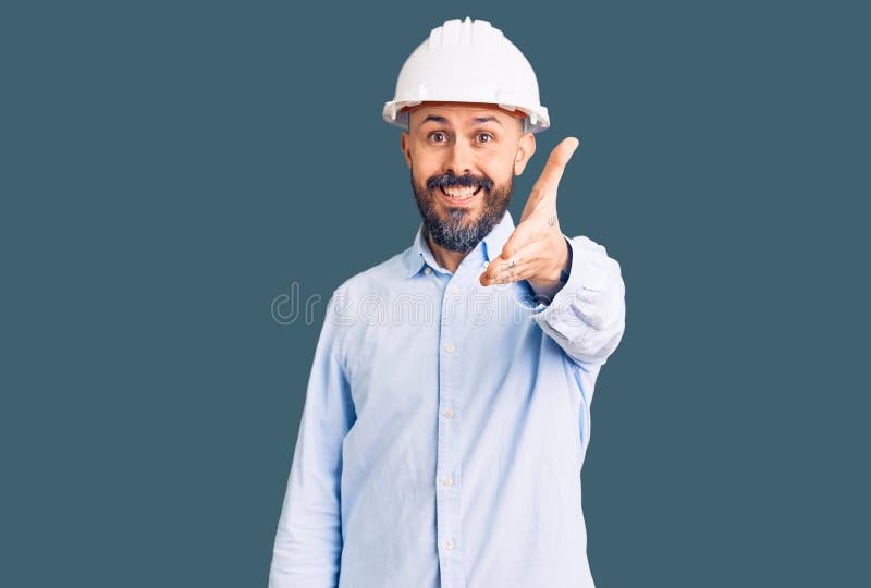 年轻帅气的建筑师戴着硬帽，微笑着友好地表示问候和欢迎 库存照片