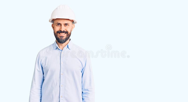年轻帅气的男人，戴着建筑师的硬帽，脸上带着快乐而酷笑 免版税库存照片
