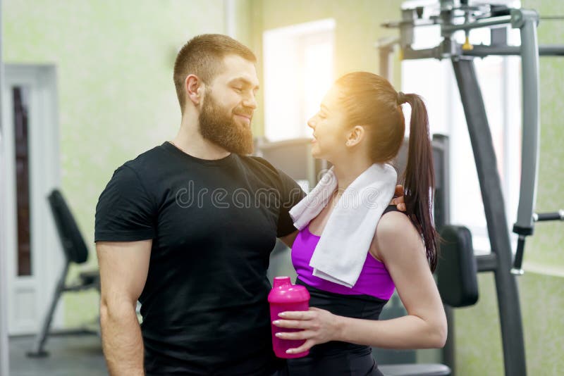 年轻愉快微笑的男人和妇女谈的拥抱在健身房 体育、训练、家庭和健康生活方式 库存图片 年轻愉快微笑的男人和妇女谈的拥抱在健身房 体育、训练、家庭和健康生活方式 库存图片