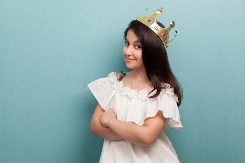 年轻满意的傲慢美丽的公主画象在白色礼服佩带和金黄王冠冠、身分和横渡的胳膊, 免版税图库摄影 年轻满意的傲慢美丽的公主画象在白色礼服佩带和金黄王冠冠、身分和横渡的胳膊, 免版税图库摄影