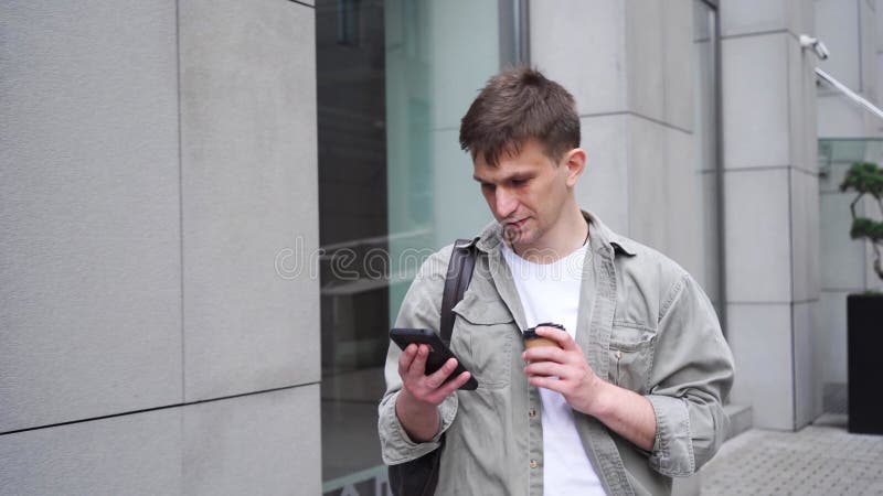 年轻的男性企业家带着智能手机和一杯咖啡在大都市漫步.