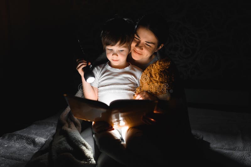 Happy family. Time for stories. Delighted happy cute m and son enjoying a book before sleeping and using a flashlight. Happy family. Time for stories. Delighted happy cute m and son enjoying a book before sleeping and using a flashlight.