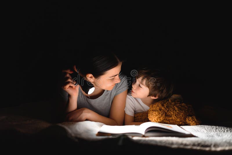 Happy family. Time for stories. Delighted happy cute m and son enjoying a book before sleeping and using a flashlight. Happy family. Time for stories. Delighted happy cute m and son enjoying a book before sleeping and using a flashlight.