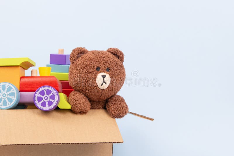 幼儿玩具背景. 淡蓝色背景中棕色硬纸板箱中的泰迪熊和教育用木玩具 库存图片