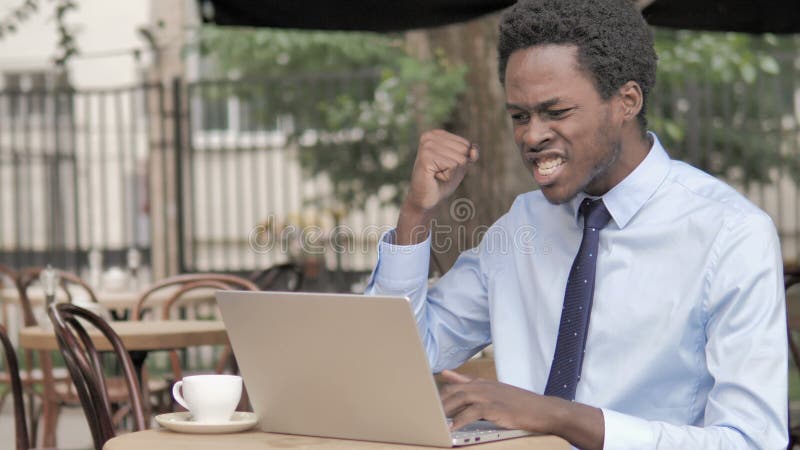 庆祝在室外咖啡馆的膝上型计算机的非洲商人