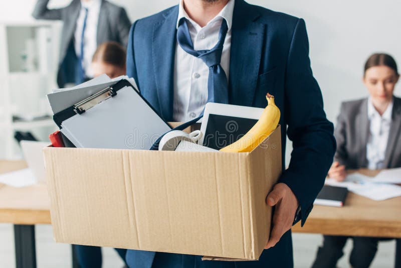 Selective focus of dismissed man holding cardboard box with papers, digital tablet and banana in office. Selective focus of dismissed man holding cardboard box with papers, digital tablet and banana in office