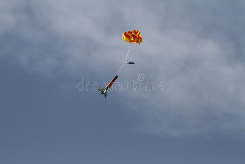 A model rocket floats down from the sky under a parachute. A model rocket floats down from the sky under a parachute
