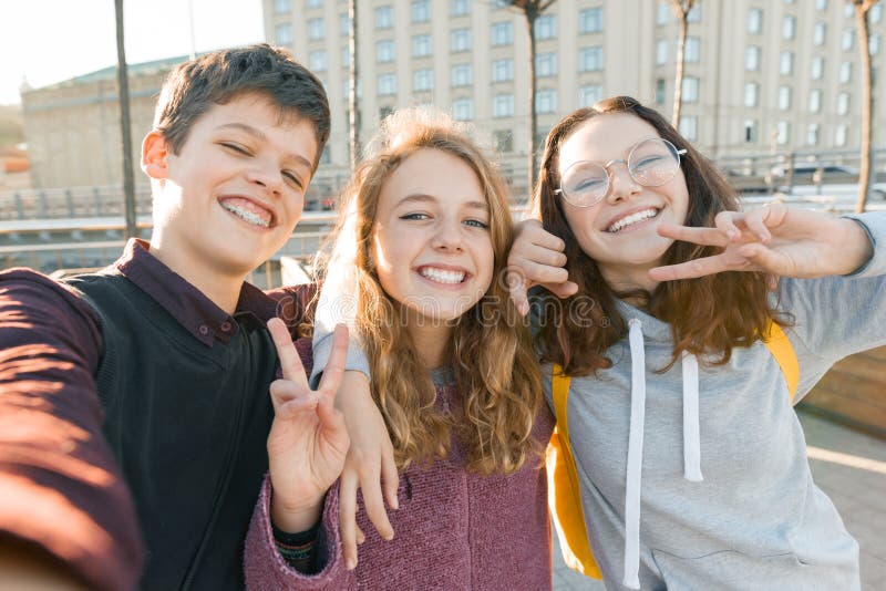  微笑和采取selfie的三個青少年的朋友男孩和兩個女孩畫象戶外 城市背景，金黃小時 庫存照片