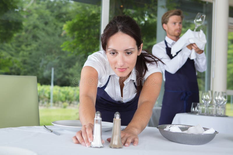 微笑的服务员在餐厅摆放餐具 免版税库存图片