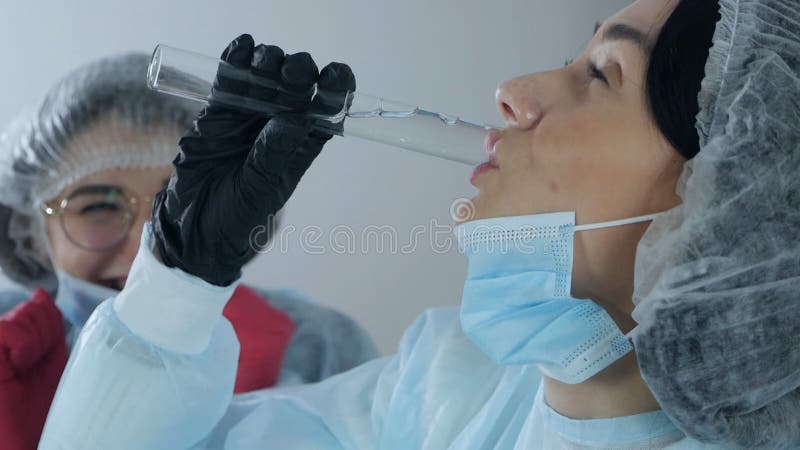 快乐的医生. 身穿蓝色外套的科学女医生在工业实验室从一个玻璃瓶里喝着液体