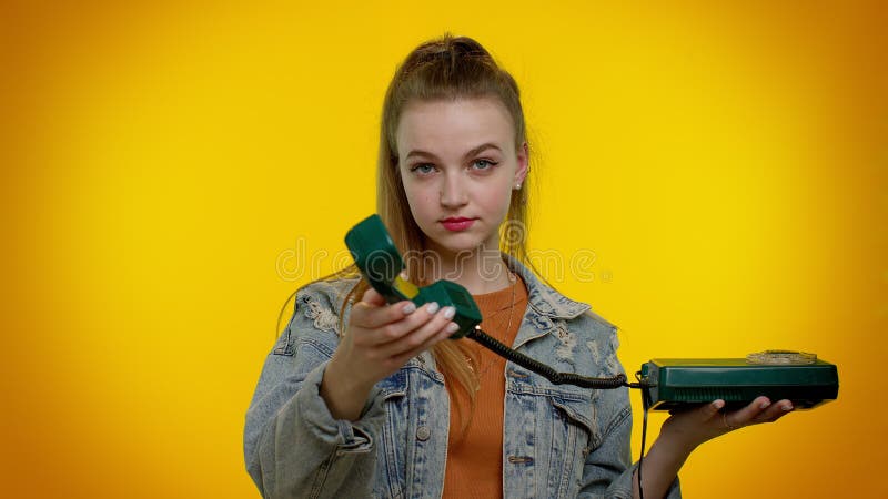 Hey you, call me back. Cheerful teen girl secretary in denim jacket talking on wired vintage telephone of 80s, says hey you call me back. Young woman posing isolated on yellow studio wall background. Hey you, call me back. Cheerful teen girl secretary in denim jacket talking on wired vintage telephone of 80s, says hey you call me back. Young woman posing isolated on yellow studio wall background