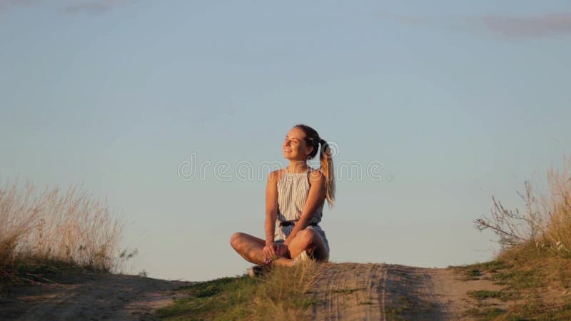 思考在落日的光芒的小山的美丽的女孩