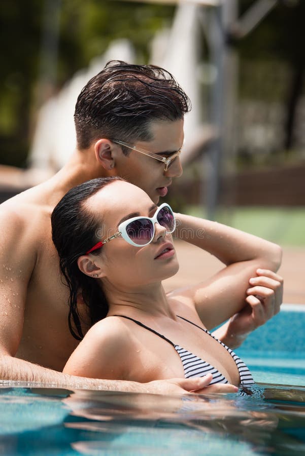 Surface level of sexy couple in sunglasses relaxing in swimming pool,stock image. Surface level of sexy couple in sunglasses relaxing in swimming pool,stock image