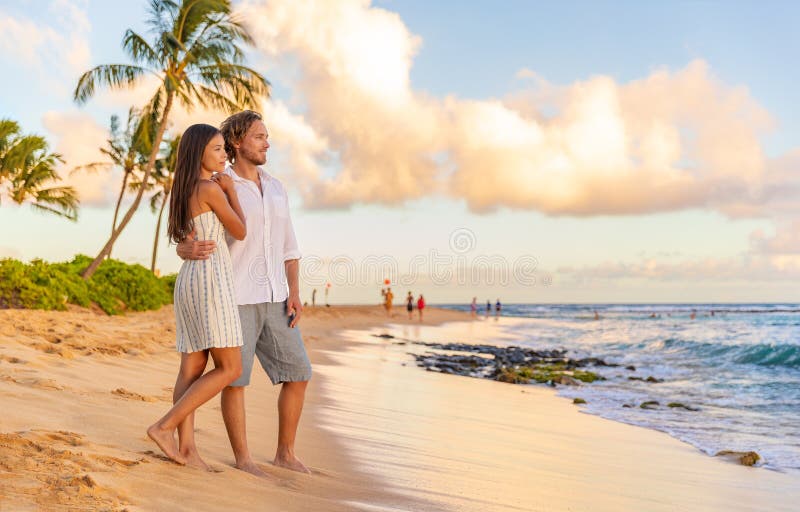 情侣们在浪漫的日落海滩漫步,在考艾岛美国度假. 亚洲女性 库存照片