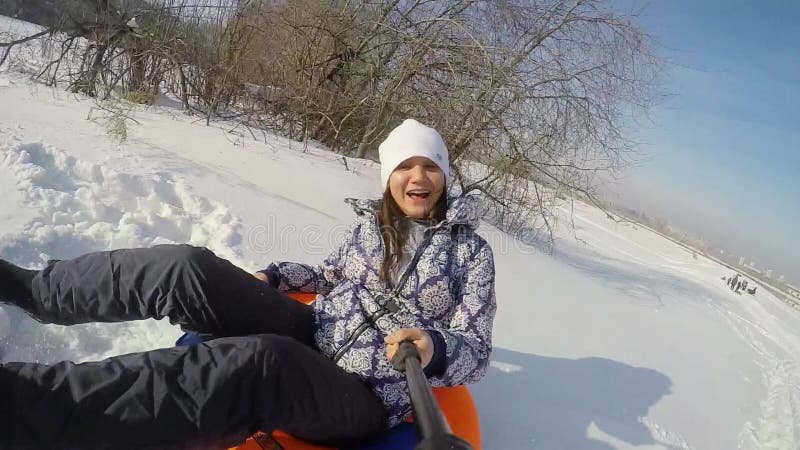 愉快的年轻逗人喜爱的妇女在山在冬天和记录sledding通过在慢动作的太阳在晴天