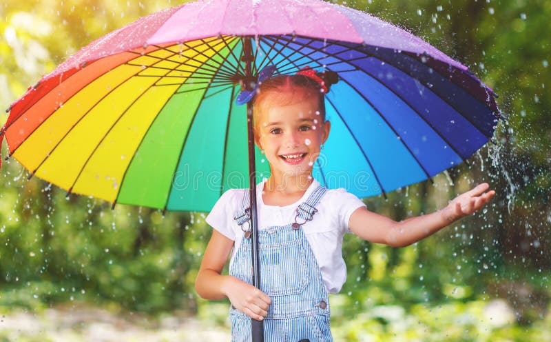 愉快的儿童女孩笑并且使用在与umbr的夏天雨下 免版税库存图片