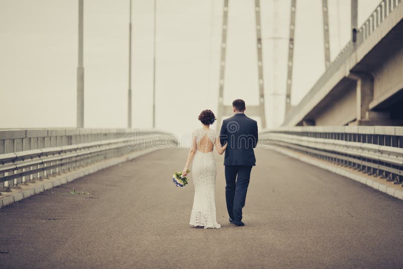 愉快的庆祝婚礼之日的新娘和新郎 走开在桥梁的已婚夫妇 长科生活路概念 定调子 库存照片 愉快的庆祝婚礼之日的新娘和新郎 走开在桥梁的已婚夫妇 长科生活路概念 定调子 库存照片