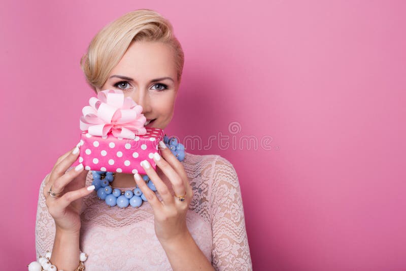 Happy birthday. Sweet blonde woman holding small gift box with ribbon. Soft colors. Studio portrait over pink background. Happy birthday. Sweet blonde woman holding small gift box with ribbon. Soft colors. Studio portrait over pink background