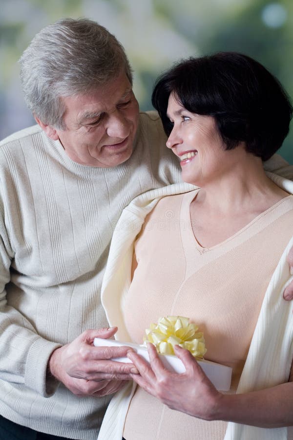 Elderly happy couple with gift box, smiling and embracing. Elderly happy couple with gift box, smiling and embracing