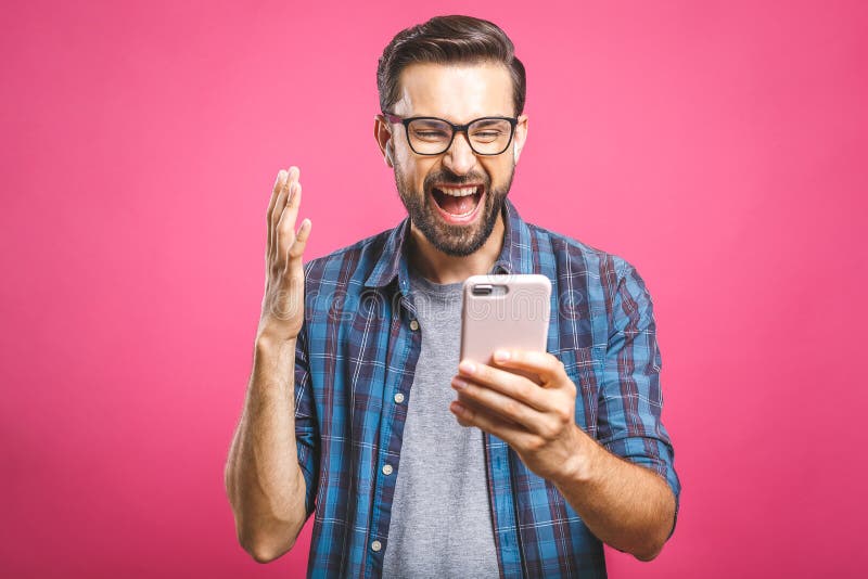 I`m a winner! Happy young handsome man holding smartphone and celebrating his success over pink background. I`m a winner! Happy young handsome man holding smartphone and celebrating his success over pink background