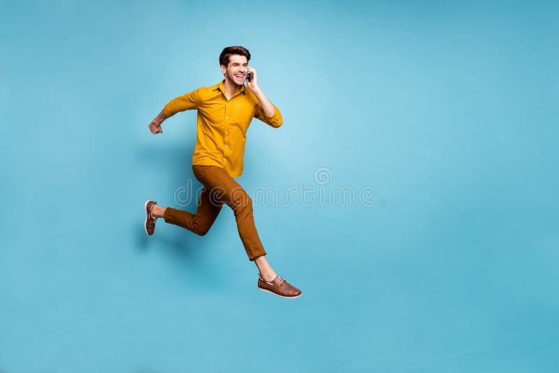 I`m on my way. Full length photo of crazy guy jumping high rushing to party holding, telephone speaking friends wear yellow shirt pants  blue color background. I`m on my way. Full length photo of crazy guy jumping high rushing to party holding, telephone speaking friends wear yellow shirt pants  blue color background