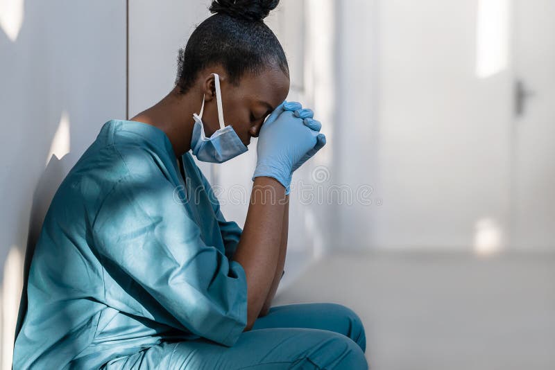 戴着口罩的疲惫抑郁的非洲女护士坐在医院的地板上 库存照片
